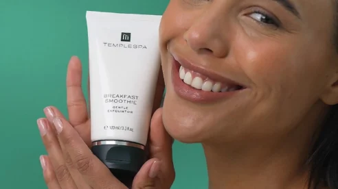 Smiling woman holding a skincare product against a green background.