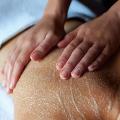 Hands applying a gentle massage scrub on a person's back in a relaxing spa setting.