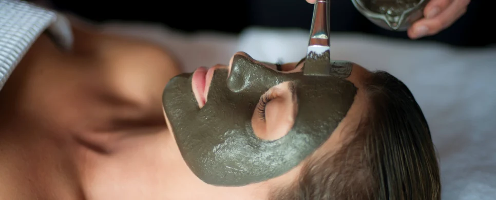 Vrouw krijgt een kalmerend moddermasker in een spa, therapeut brengt het masker aan met een kwast, ontspannen sfeer.