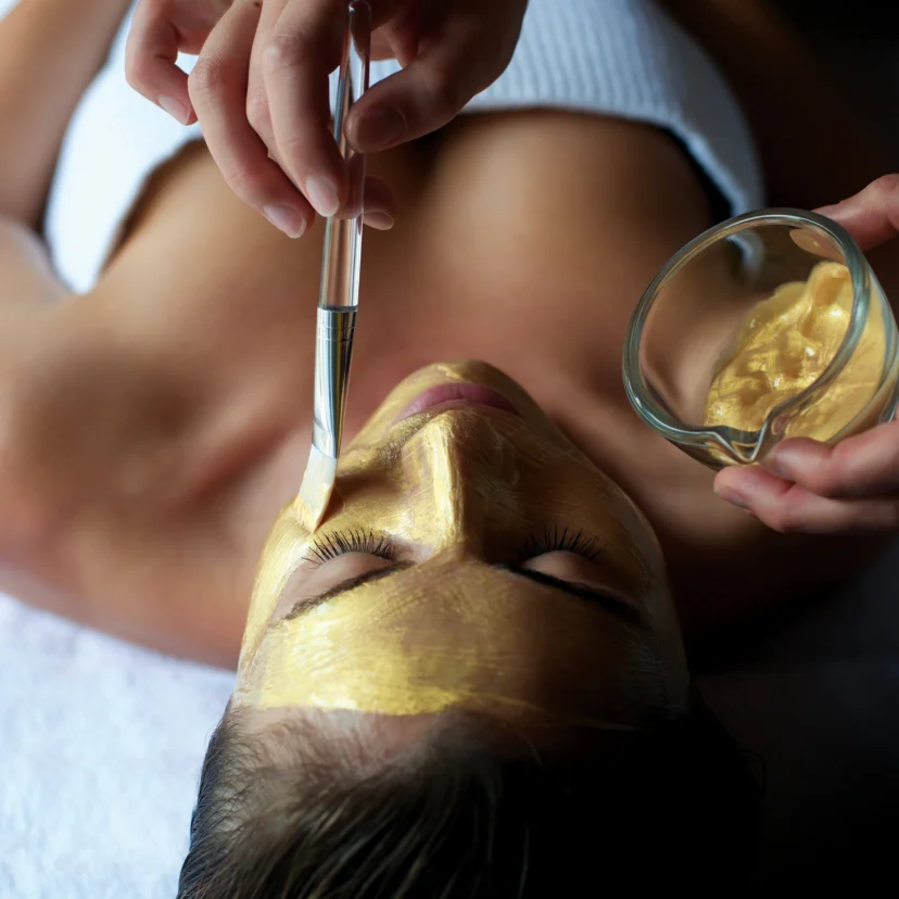 Relaxed guest receiving a golden facial mask applied with a brush at a spa, towel visible