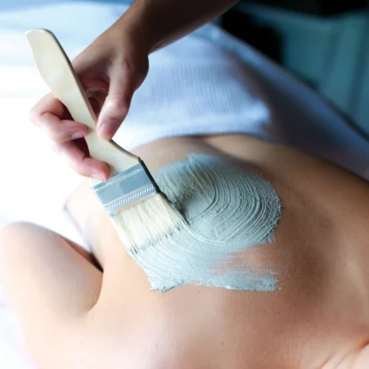 Spa treatment with a soothing mud mask being applied to a person's back in a tranquil setting.
