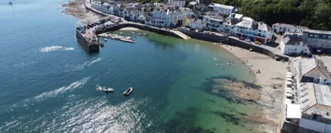 Aerial view of families enjoying a sunny day by the seaside, in a picturesque coastal village.