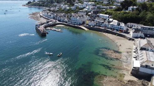 Aerial view of families enjoying a sunny day by the seaside, in a picturesque coastal village.