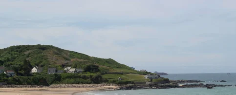 Scenic coastal view with sandy beach and green hills, ideal for family relaxation.