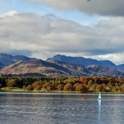 A serene lake with sailboats and lush autumn trees against a backdrop of mountains.
