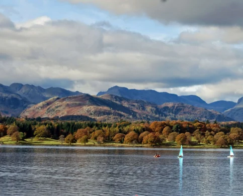 A serene lake with sailboats and lush autumn trees against a backdrop of mountains.