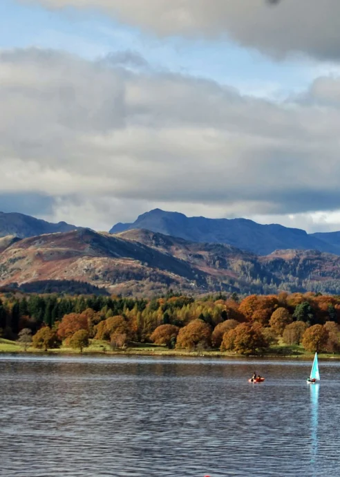 A serene lake with sailboats and lush autumn trees against a backdrop of mountains.