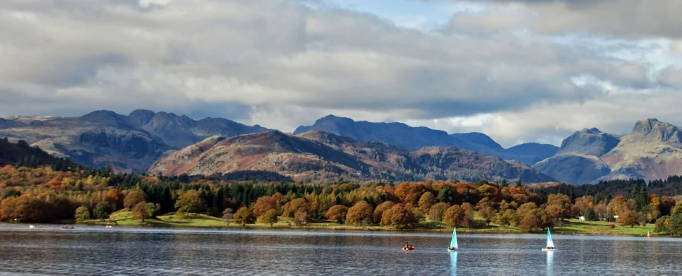 Family sailing on a peaceful lake with autumn trees and distant mountains under clouded sky