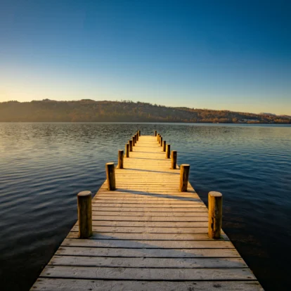 Scenic lakeside view from a wooden pier with mountains at sunset.