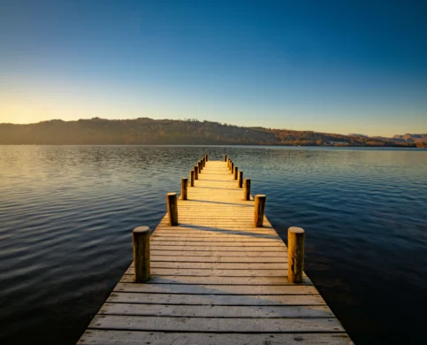 Scenic lakeside view from a wooden pier with mountains at sunset.