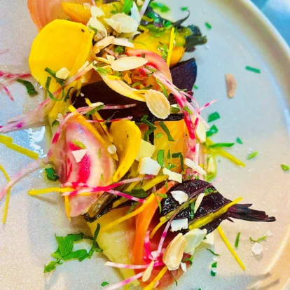 Colourful vegetable salad with shaved almonds and herbs, elegantly plated on a white dish.