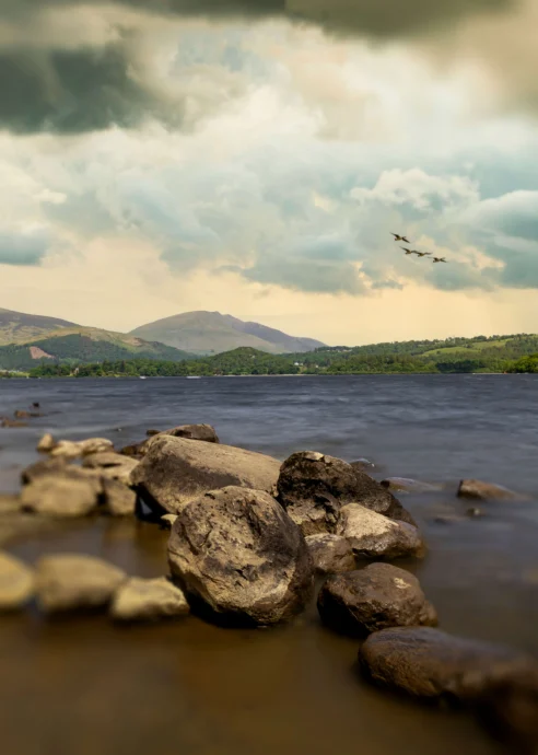 Scenic lakeside view with mountains under a cloudy sky, serene and inviting landscape.