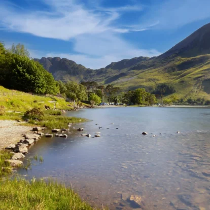 A serene lakeside view with lush hills under a clear blue sky, inviting tranquillity.