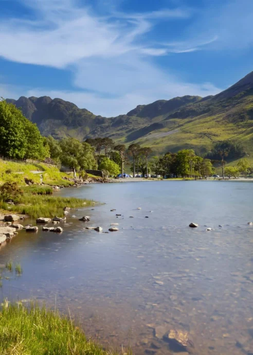 A serene lakeside view with lush hills under a clear blue sky, inviting tranquillity.