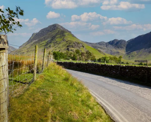 Scenic countryside road by lush hills under a clear blue sky, inviting for a peaceful escape.
