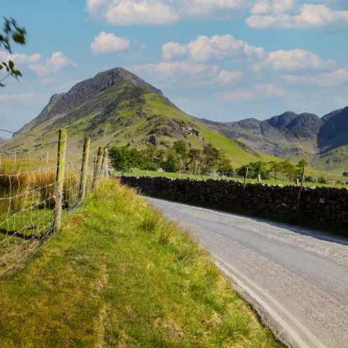 Scenic countryside road by lush hills under a clear blue sky, inviting for a peaceful escape.