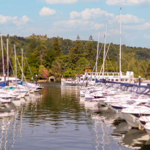 Idyllic marina scene with families exploring yachts, surrounded by serene water and lush hills.