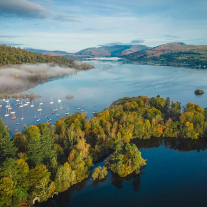 Aerial view of a serene lake with moored boats and autumn-coloured trees surrounding the water.