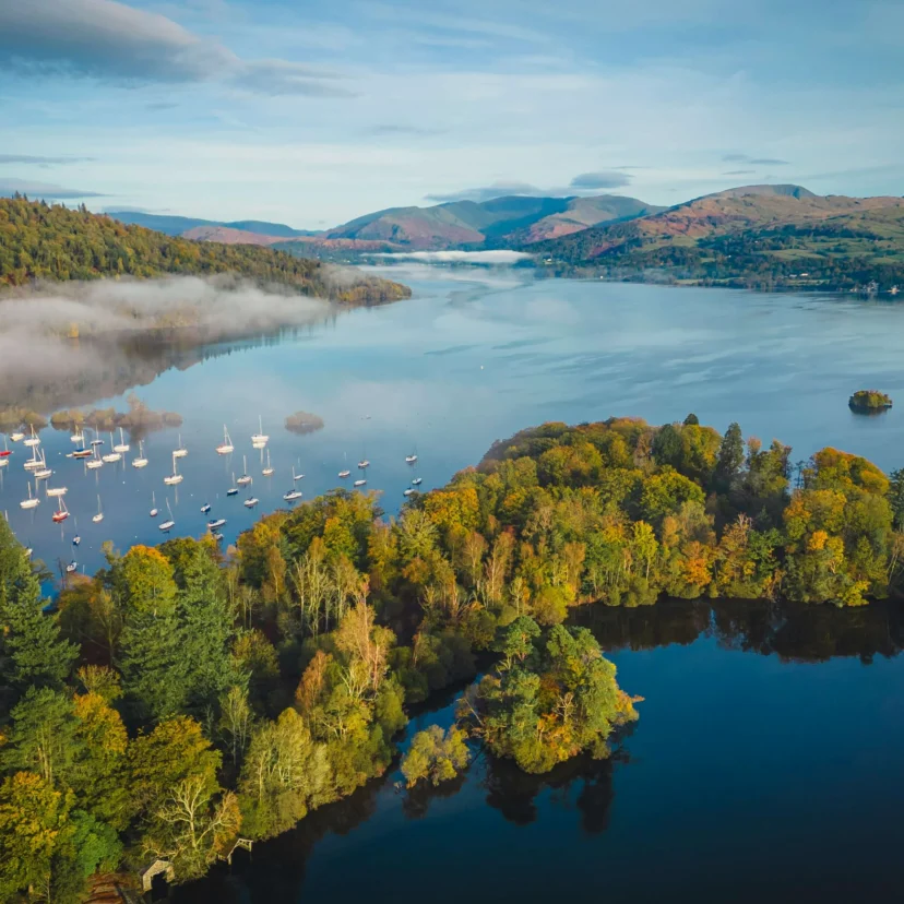 Family enjoying sailboats and lakeside autumn woodland with mist over a peaceful lake (no text visible)