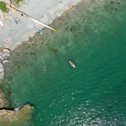 Aerial view of vibrant beach with families swimming and kayaking in clear turquoise water.