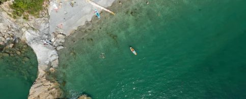Aerial view of vibrant beach with families swimming and kayaking in clear turquoise water.