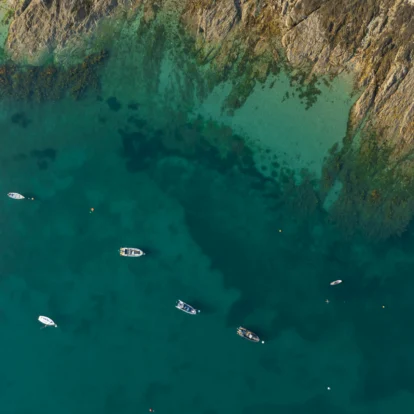 Aerial view of boats near rocky coastline in clear blue waters.