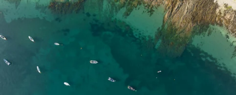 Aerial view of boats near rocky coastline in clear blue waters.