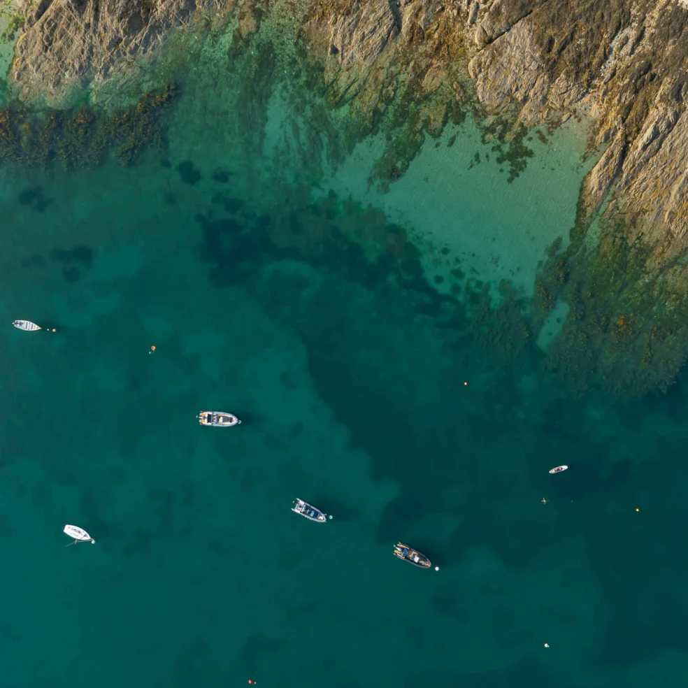 Family rowing small boats near a rocky turquoise shoreline on a calm coastal day