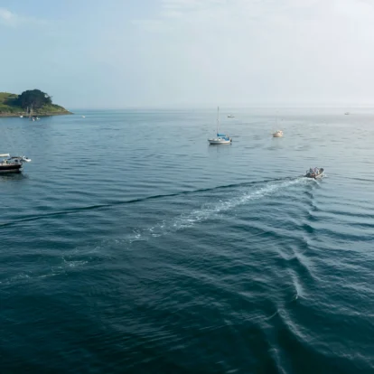 A serene sea landscape with boats and distant lush coastline under a clear sky.