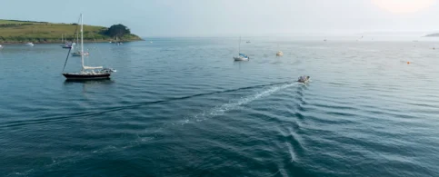 A serene sea landscape with boats and distant lush coastline under a clear sky.