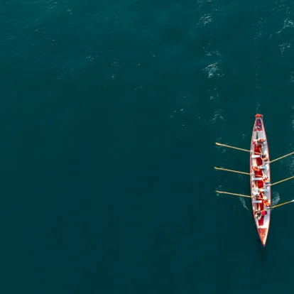 A family rowing a longboat together on calm blue waters, enjoying a sunny day.