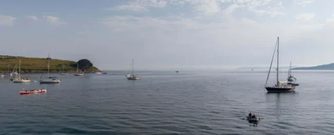 A family enjoys canoeing on a serene ocean near a lush, green coastline under a clear sky.