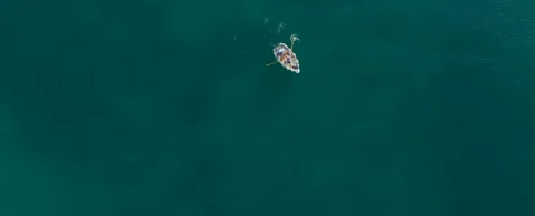 Aerial view of a family in a small boat on calm, turquoise sea, enjoying a sunny day.