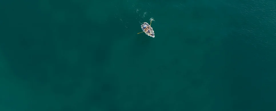 Small family rowing a dinghy together on calm deep teal sea, leisurely holiday moment