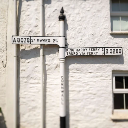 Rustic white building with vintage directional signs to St. Mawes and King Harry Ferry.