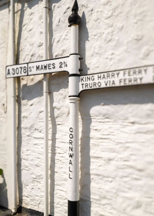 Vintage signpost pointing to St Mawes and King Harry Ferry, set against a charming white-washed cottage.