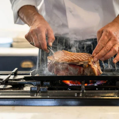 Chef searing a thick steak on a hot griddle in a hotel kitchen, family dining experience