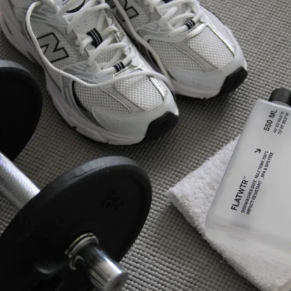 White trainers, dumbbell and water bottle on a textured mat suggesting a family's in-room workout setup, visible text "550 ML" on bottle
