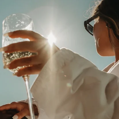 Family member on a sunlit balcony raising a wine glass, relaxed resort stay, blue sky