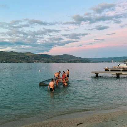 Family group playing on a lakeside platform at sunset, hills and pastel sky above (transcription: none)