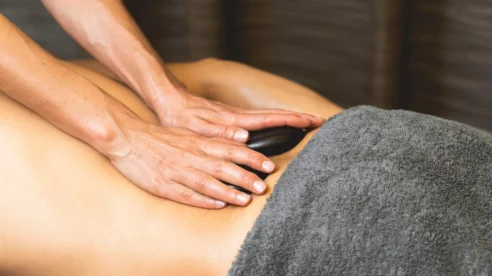 Family couple enjoying a relaxing hot stone back massage in a cosy spa treatment room, grey towel visible